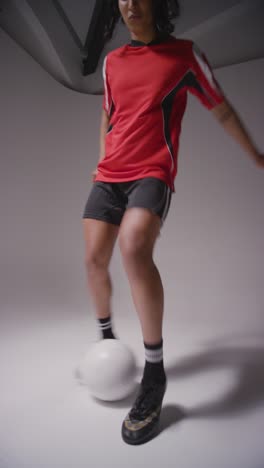 Vertical-Video-Studio-Shot-Of-Female-Footballer-Wearing-Club-Kit-Against-Grey-Background-Controlling-Ball